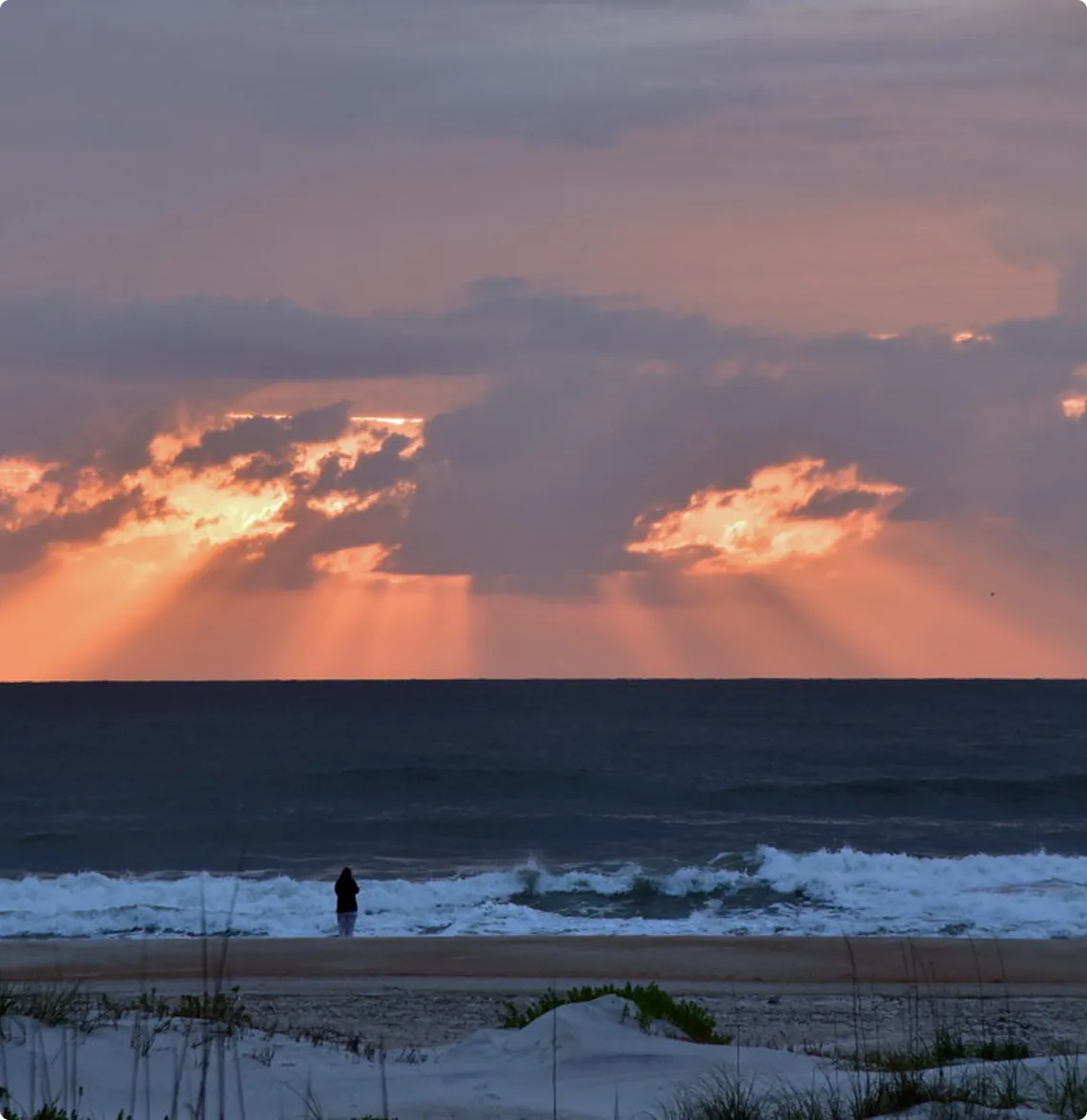 Sunset over ocean with person on shore.