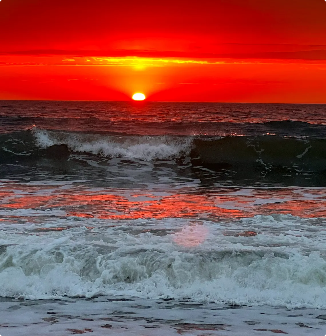 Sunset over ocean with vibrant red sky.