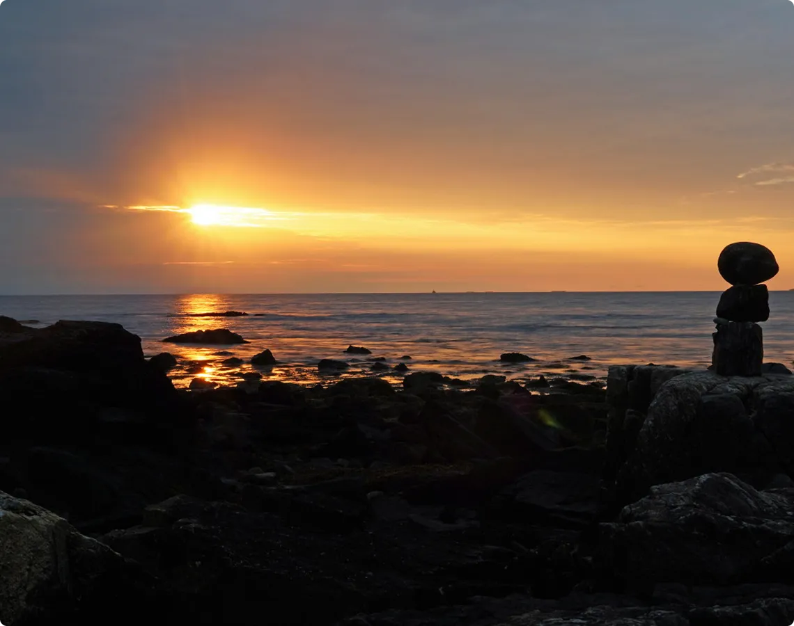Sunset over rocky shore with statue silhouette.